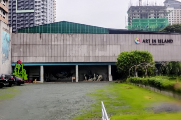 The grey Art in Island building with its sign and green roof, seen across the car park.