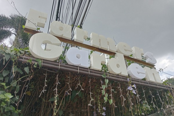 The white Farmers Garden sign above a wall of hanging vines and flowers.