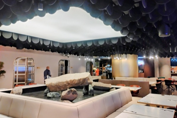 Inside World Kitchens: cream booth seating around a rock and water centrepiece under a dark scalloped ceiling.